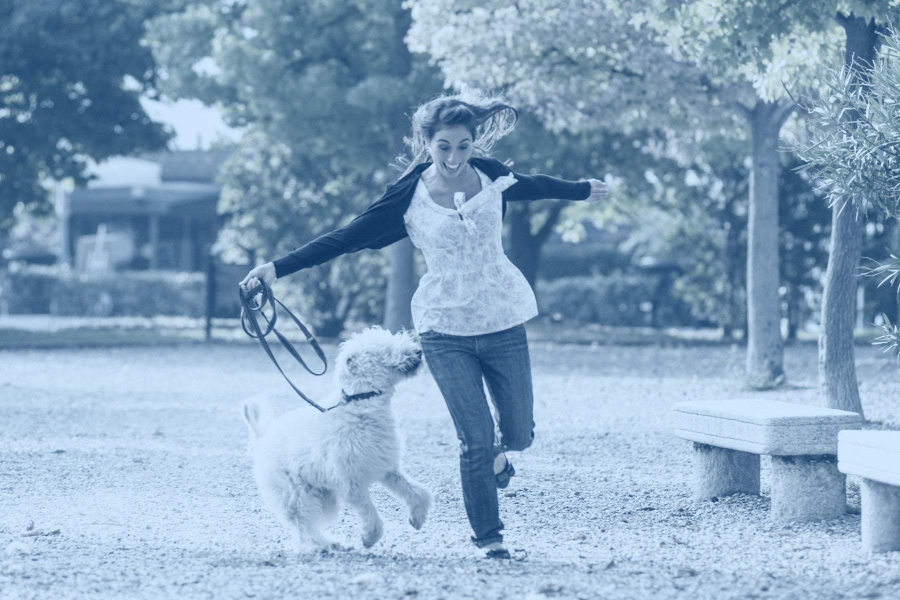 Women runs through a park with her white fluffy dog